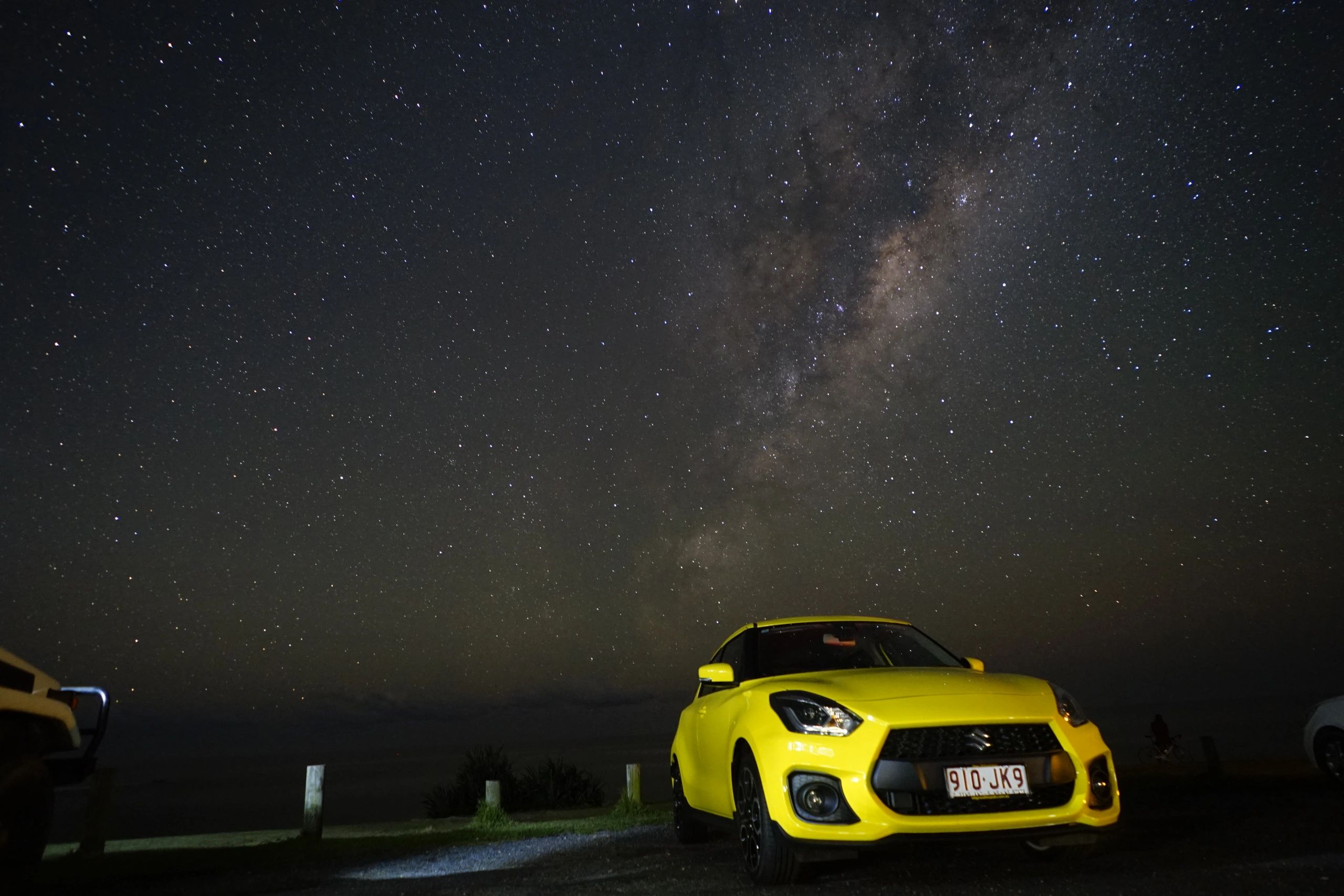 A yellow car under a starry night sky with the Milky Way visible.