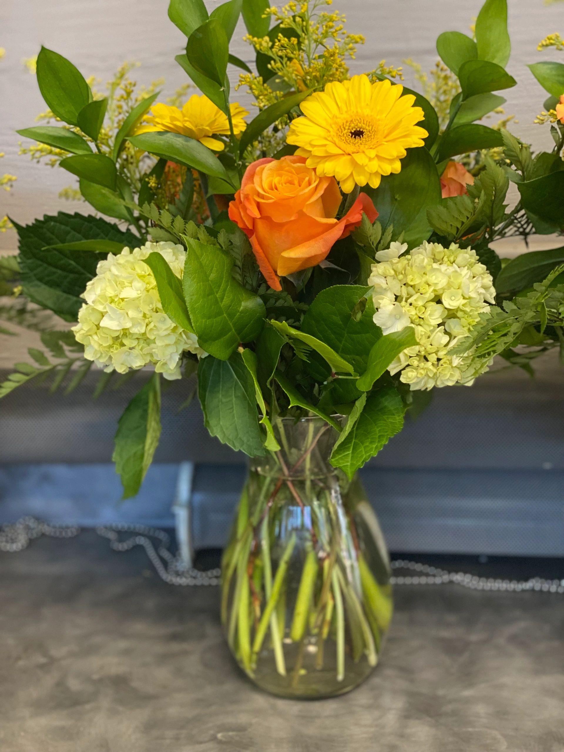 A vibrant bouquet of yellow, orange, and cream flowers in a clear glass vase.