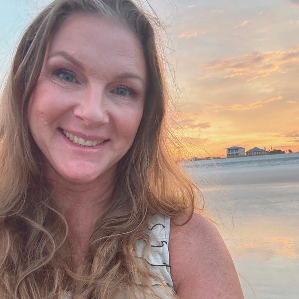 Smiling woman takes selfie at beach during sunset.