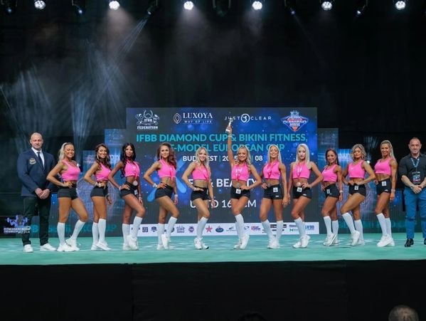 Group of bikini fitness competitors posing on stage.