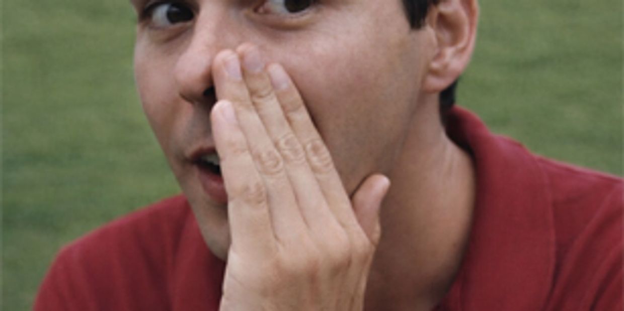 Man whispering a secret outdoors, wearing a red polo shirt.