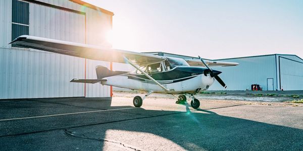 Small single-engine airplane parked near hangars at sunrise.