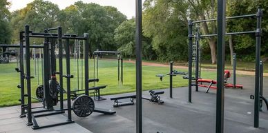 Outdoor gym area with various exercise equipment surrounded by trees.