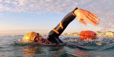 Swimmer in wetsuit and cap swimming in open water during sunrise or sunset.