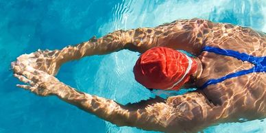 Swimmer in blue swimsuit and red cap stretches in pool water.