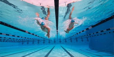 Two swimmers race side by side underwater in a pool lane.