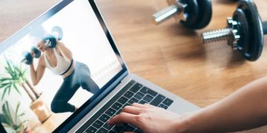 Person following an online workout on a laptop with dumbbells nearby.
