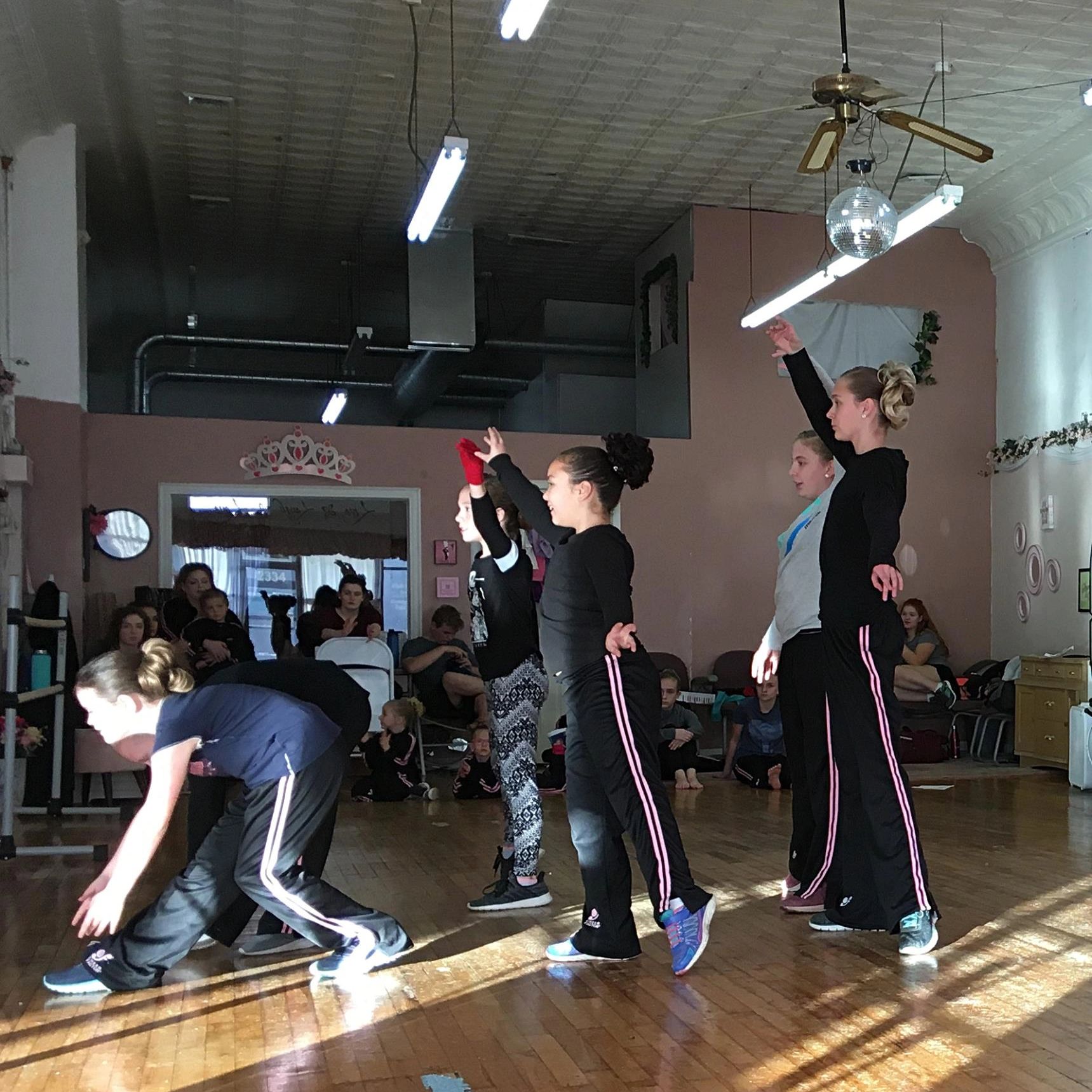 Group of children practicing dance in a studio with onlookers.