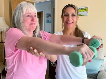 pensioner lady with personal trainer lifting dumbbells