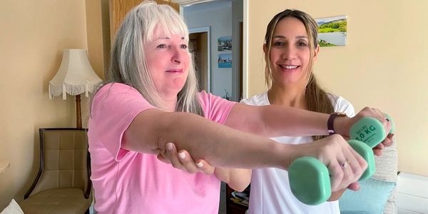 A personal trainer helping a pensioner lift dumbbells and exercising