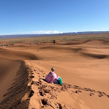 Woman sitting on sand dunes during Sahara desert retreat in Morocco, experiencing silence and medita