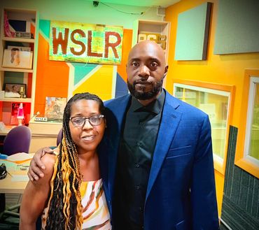 Two people posing inside a colorful radio station studio with WSLR signage.