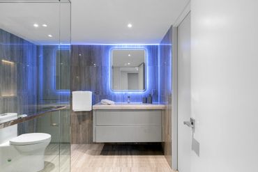 Modern bathroom with blue LED-lit mirror and glass shower enclosure.