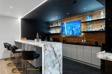 Modern marble bar with black chairs and illuminated wooden shelves.