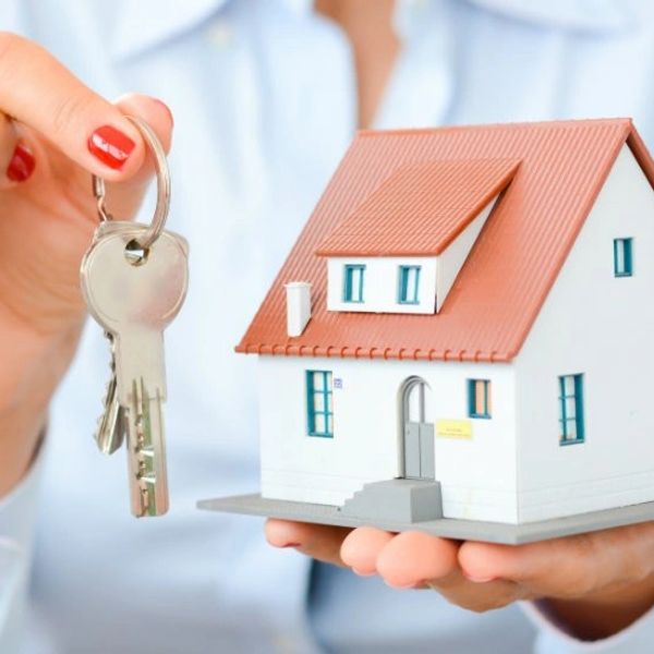 Person holding house keys and a model house in their hands.