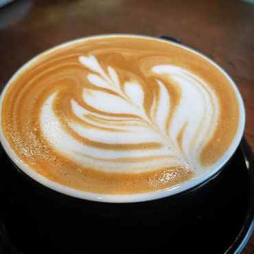 A cup of latte with intricate leaf-shaped latte art on top.