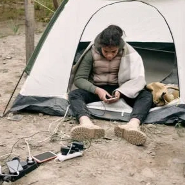 A homeless young Hispanic girl sitting in a tent using a charging strip to charge her phone outside
