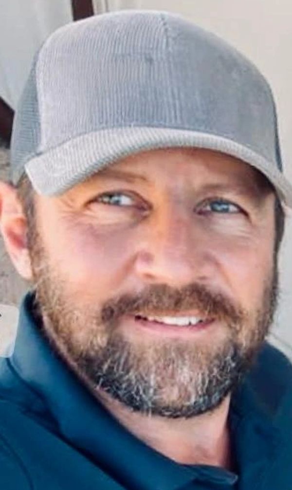 Smiling man with a beard wearing a gray cap and dark shirt.