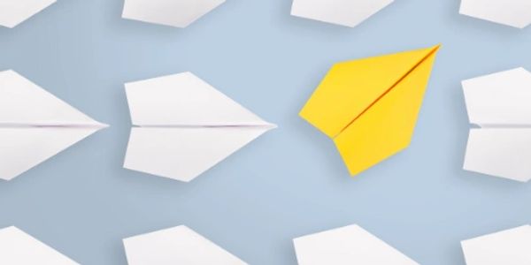 A yellow paper airplane stands out among white paper airplanes on a blue background.