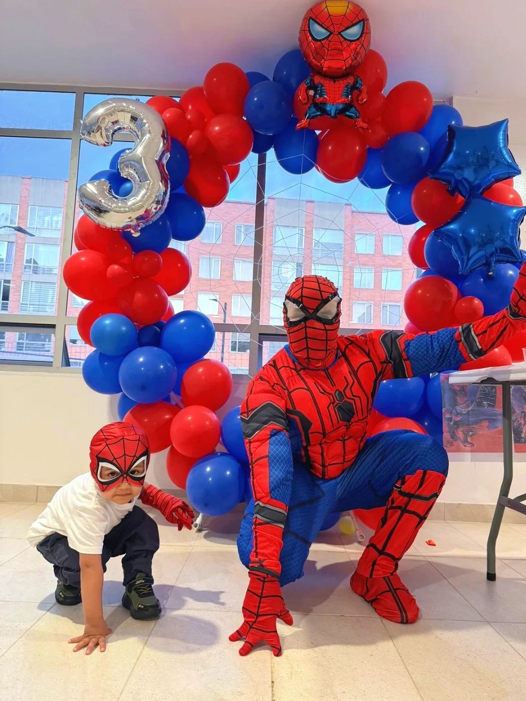 Child and adult dressed as Spider-Man at a colorful birthday party.