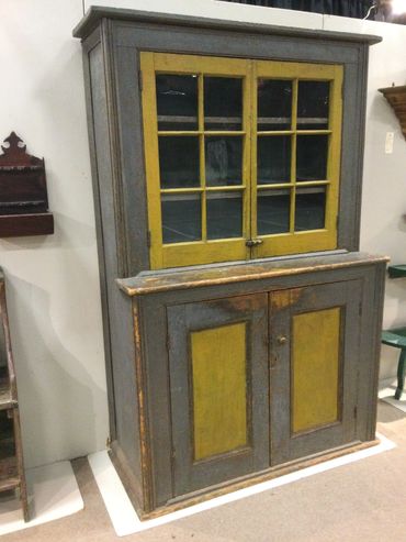 Vintage two-tone wooden cabinet with glass-paneled upper doors and solid lower doors.