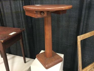 A wooden pedestal table with a triangular top and square base.