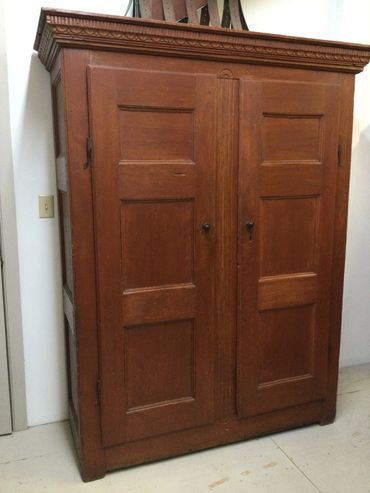 Large wooden antique wardrobe with paneled doors and ornate top molding.
