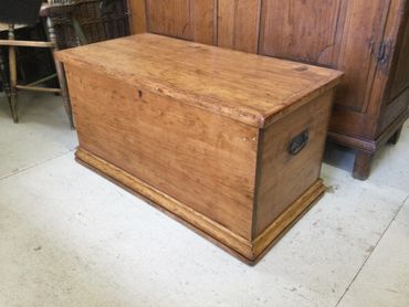 A wooden storage chest with metal handles on a light floor.