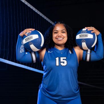 Smiling volleyball player holding two balls by the net.