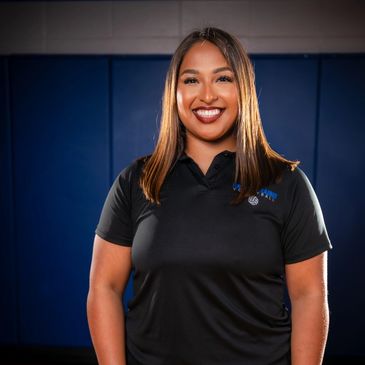Smiling woman in a black polo shirt against a blue background.