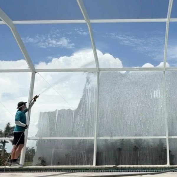 Man cleaning large glass with pressure washer.