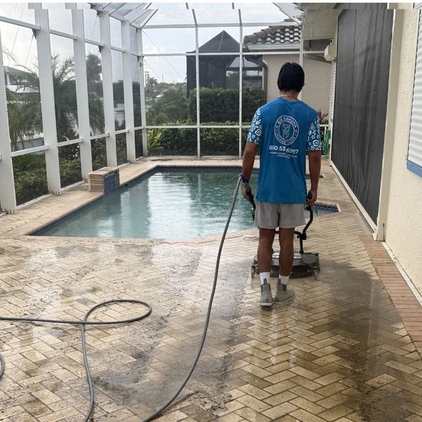 Person cleaning tiled poolside patio with power washer.