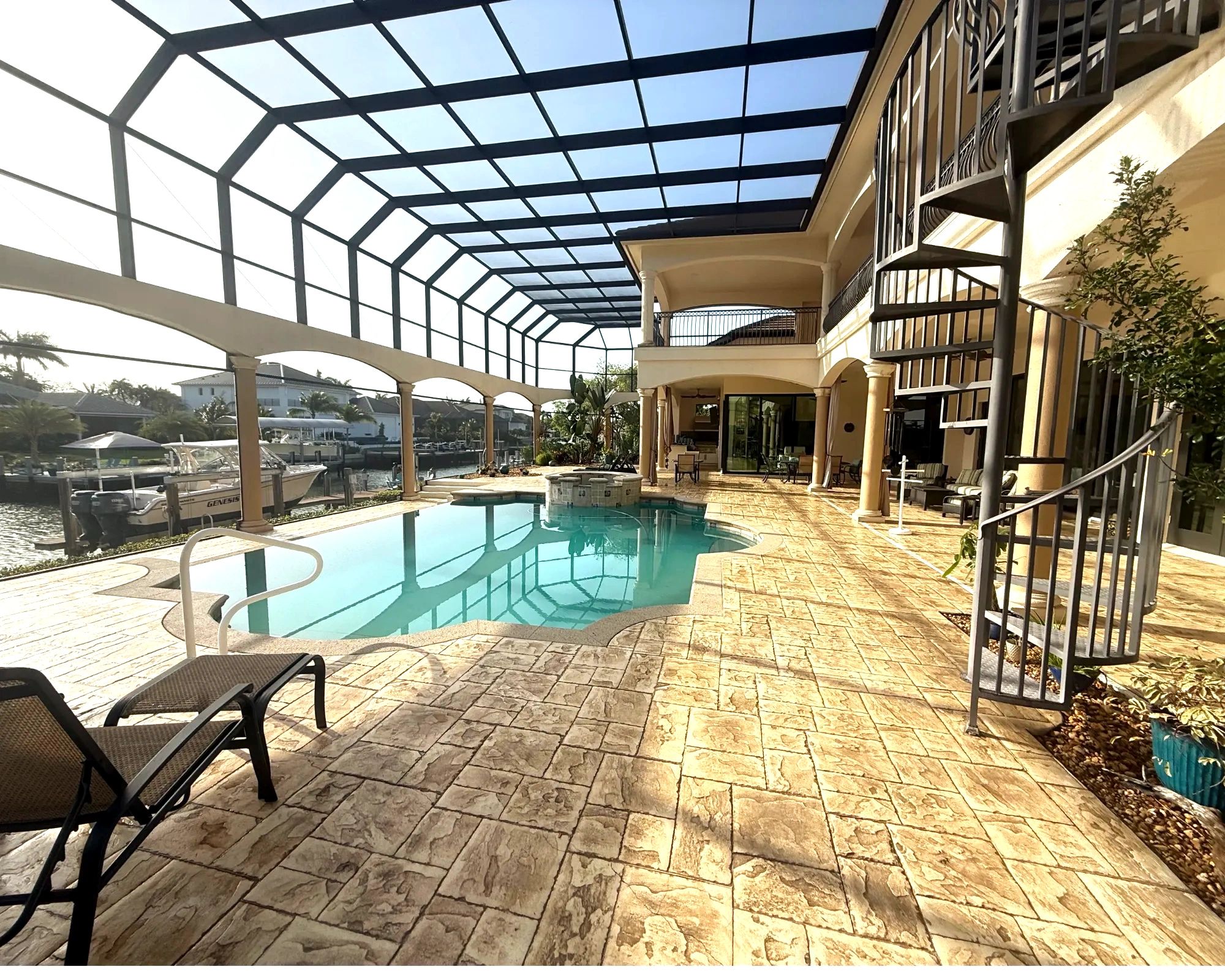 Covered outdoor pool area with spiral staircase and waterfront view.