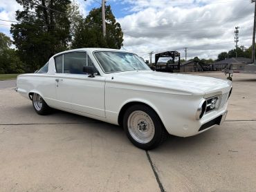 White vintage car parked on pavement under cloudy sky.