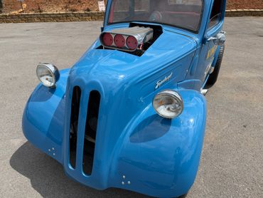 A blue vintage car with a modified engine protruding from the hood.