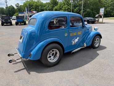 Blue vintage drag racing car named 'King Rat' with wide rear tires and side exhaust pipes.