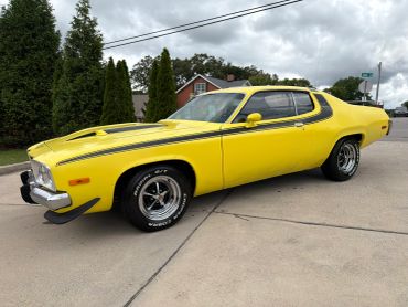 Bright yellow classic muscle car parked on driveway under cloudy sky.