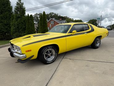Bright yellow classic muscle car parked on driveway under cloudy sky.