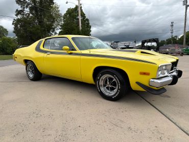 Yellow vintage muscle car with black racing stripes parked outdoors.