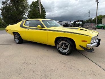Yellow vintage muscle car with black racing stripes parked outdoors.