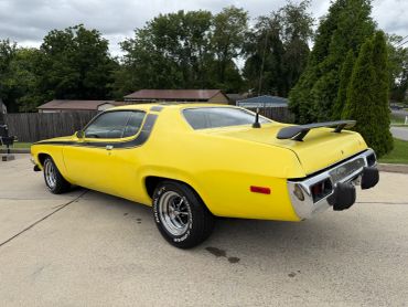 Yellow vintage muscle car parked on a driveway under a cloudy sky.