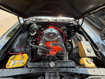 Car engine bay with orange engine block and yellow car battery.