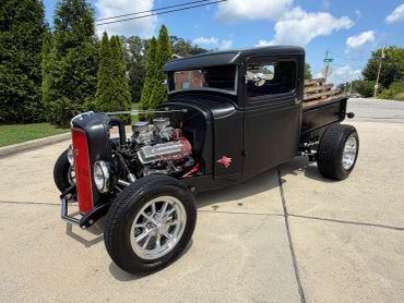 Matte black vintage hot rod truck with large engine and shiny wheels.
