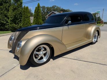 Classic custom beige and black vintage car with shiny chrome rims.