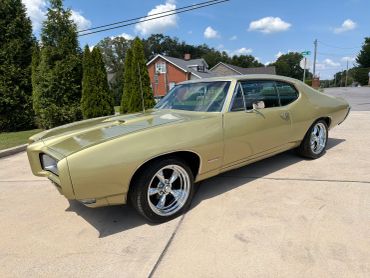 Classic beige muscle car parked on driveway under blue sky.