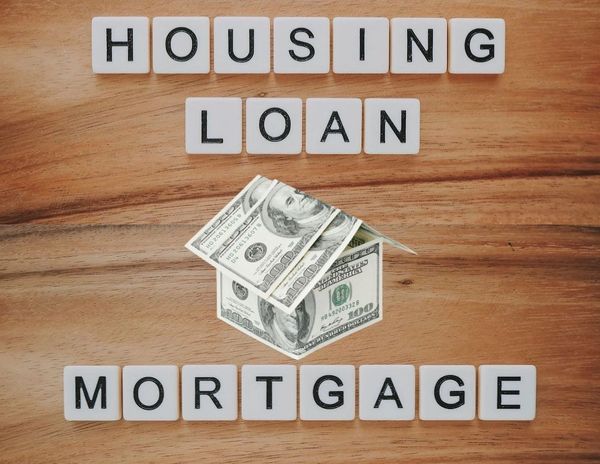 the words housing loan and mortgage with the image of tented $100 bills in the shape of a house. 
