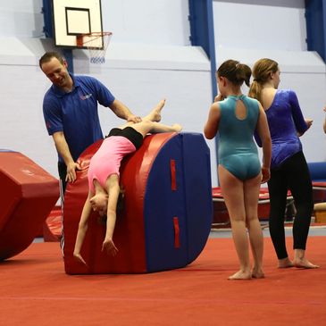 A gymnastics instructor helping a child to roll on their arms