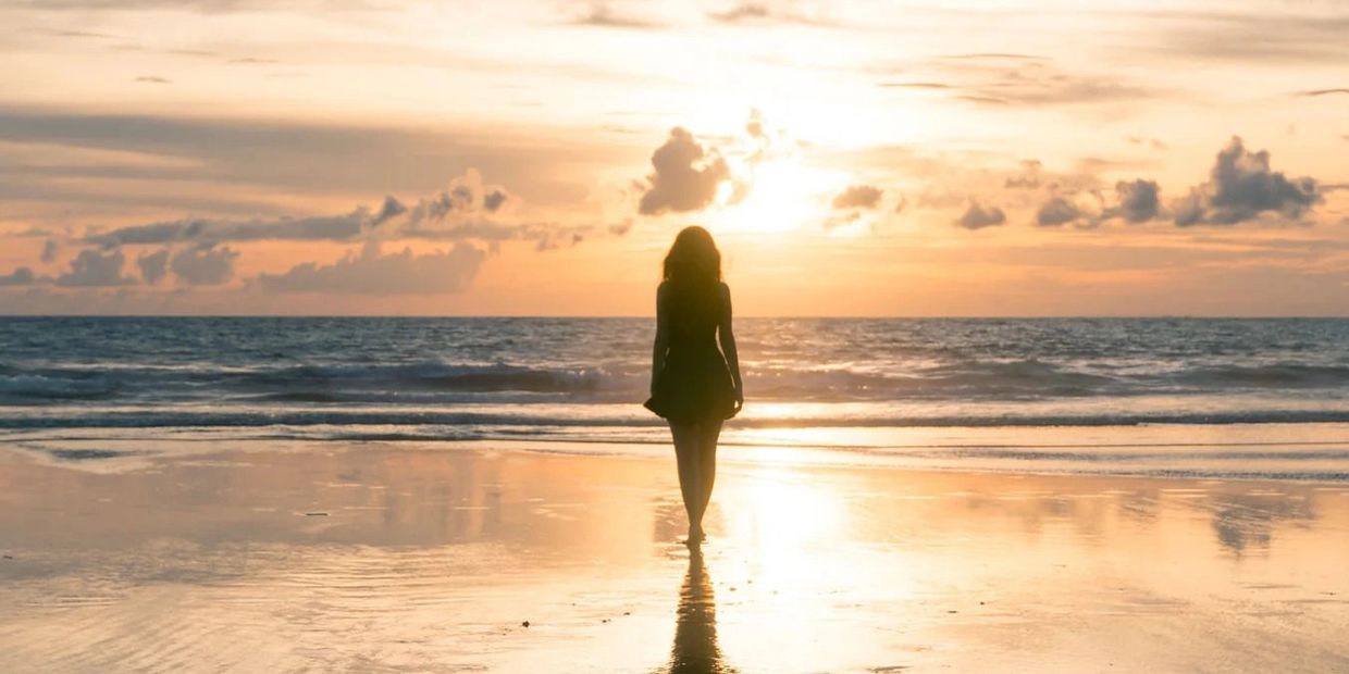 Silhouette of a woman walking on the beach at sunset.
