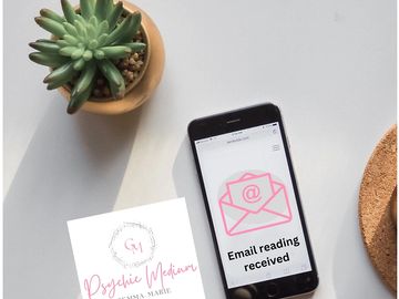 A smartphone showing an email notification beside a Psychic Medium business card and a small succulent plant.