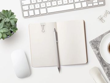 Minimalist workspace with blank notebook, pen, keyboard, mouse, coffee, and succulent plant.